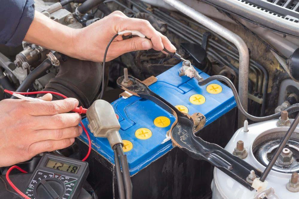 Battery being tested with a multimeter showing 12.18 volts in an engine bay